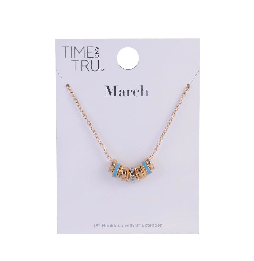 A gold chain necklace with a letter pendant spelling 'March' in gold, accented with light blue enamel details, displayed on a white Time and Tru brand card.