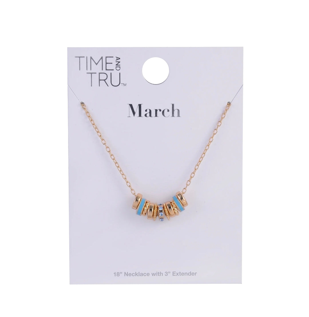 A gold chain necklace with a letter pendant spelling 'March' in gold, accented with light blue enamel details, displayed on a white Time and Tru brand card.