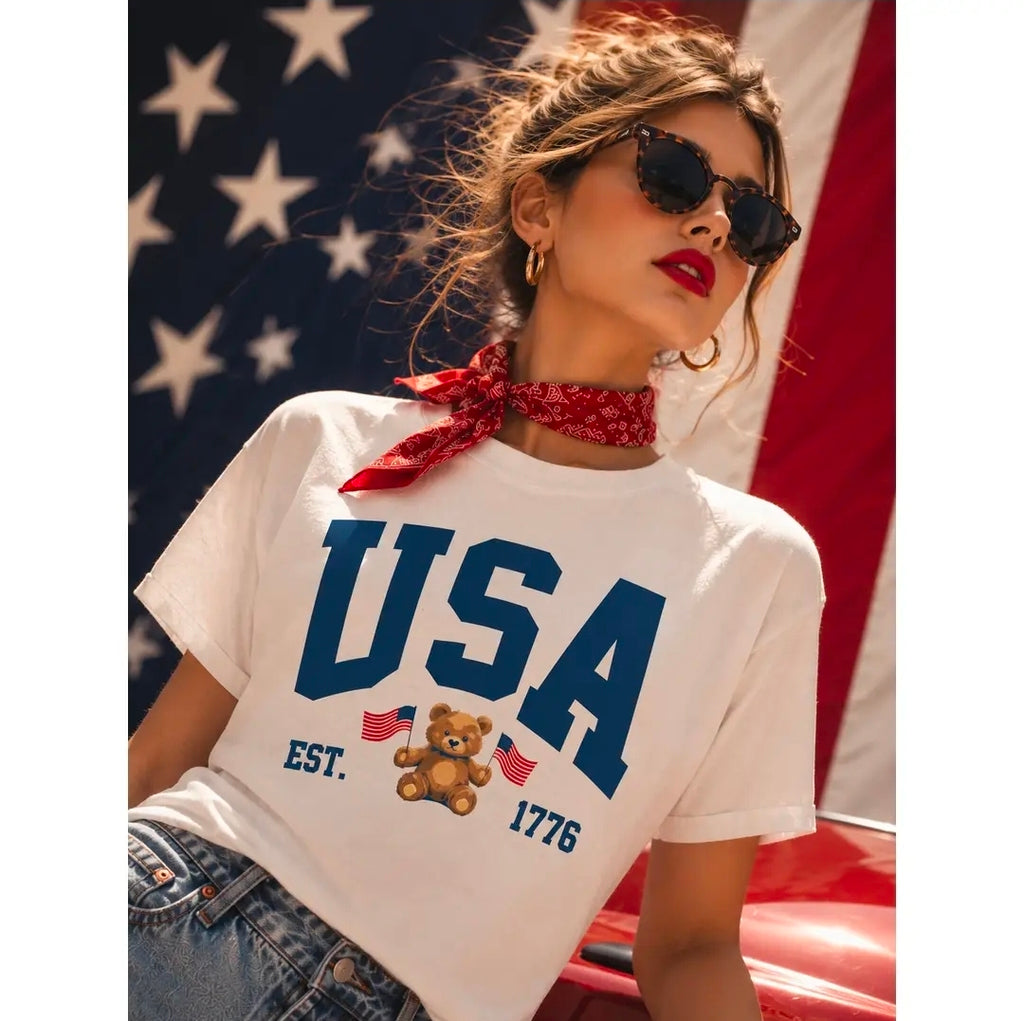 Woman wearing a white t-shirt with 'USA' and a teddy bear graphic in front of an American flag.