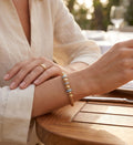 Close-up of a person's hand wearing a gold bracelet and ring on a wooden table.