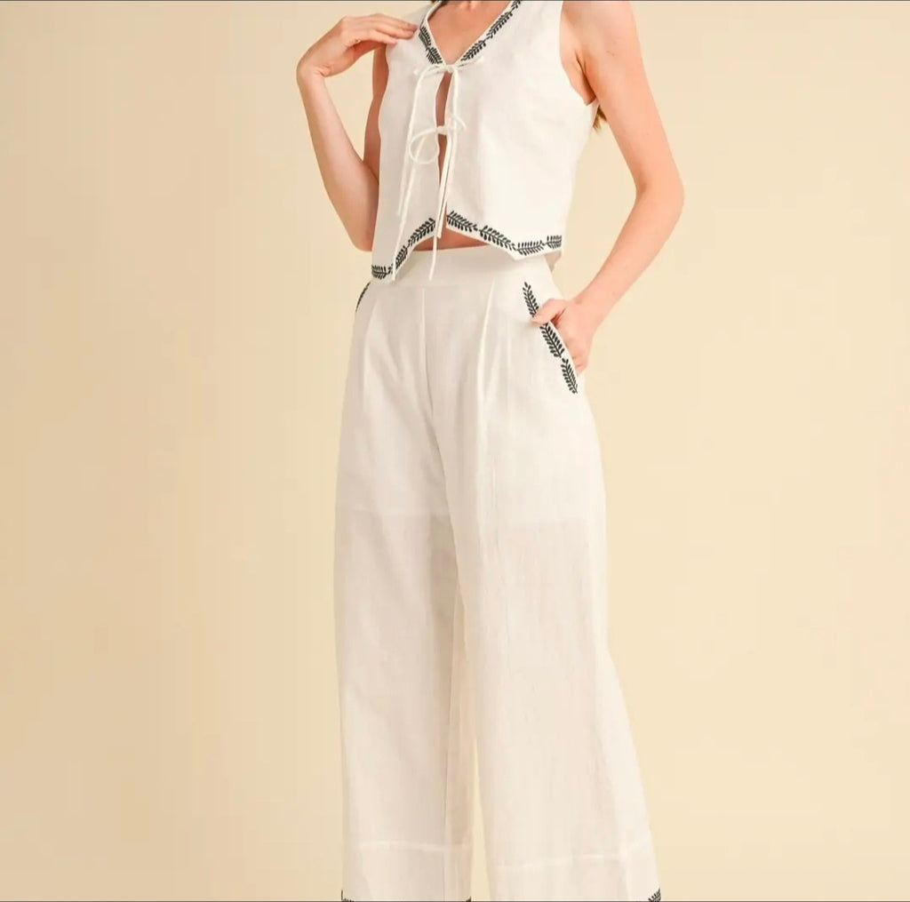 White sleeveless top and wide-leg pants with black accents on a beige background
