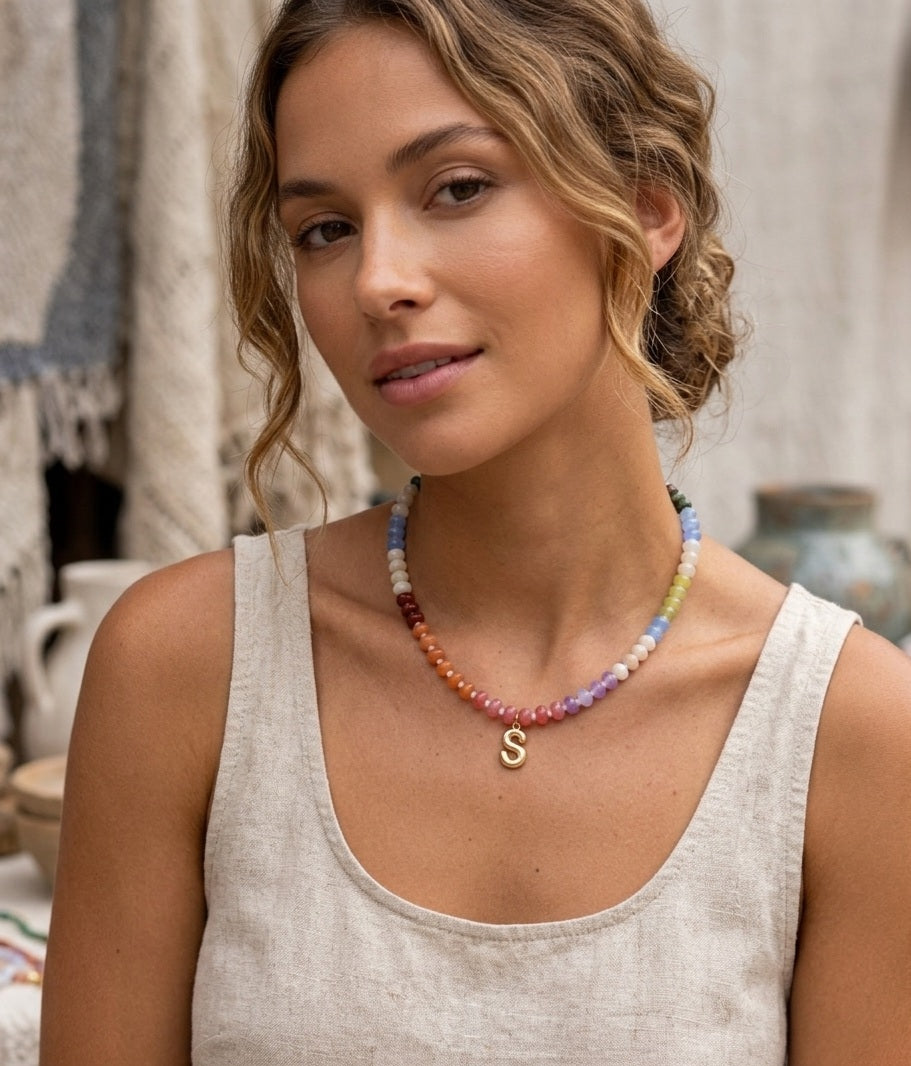 Woman wearing a colorful beaded necklace with a 'S' pendant in an outdoor setting.