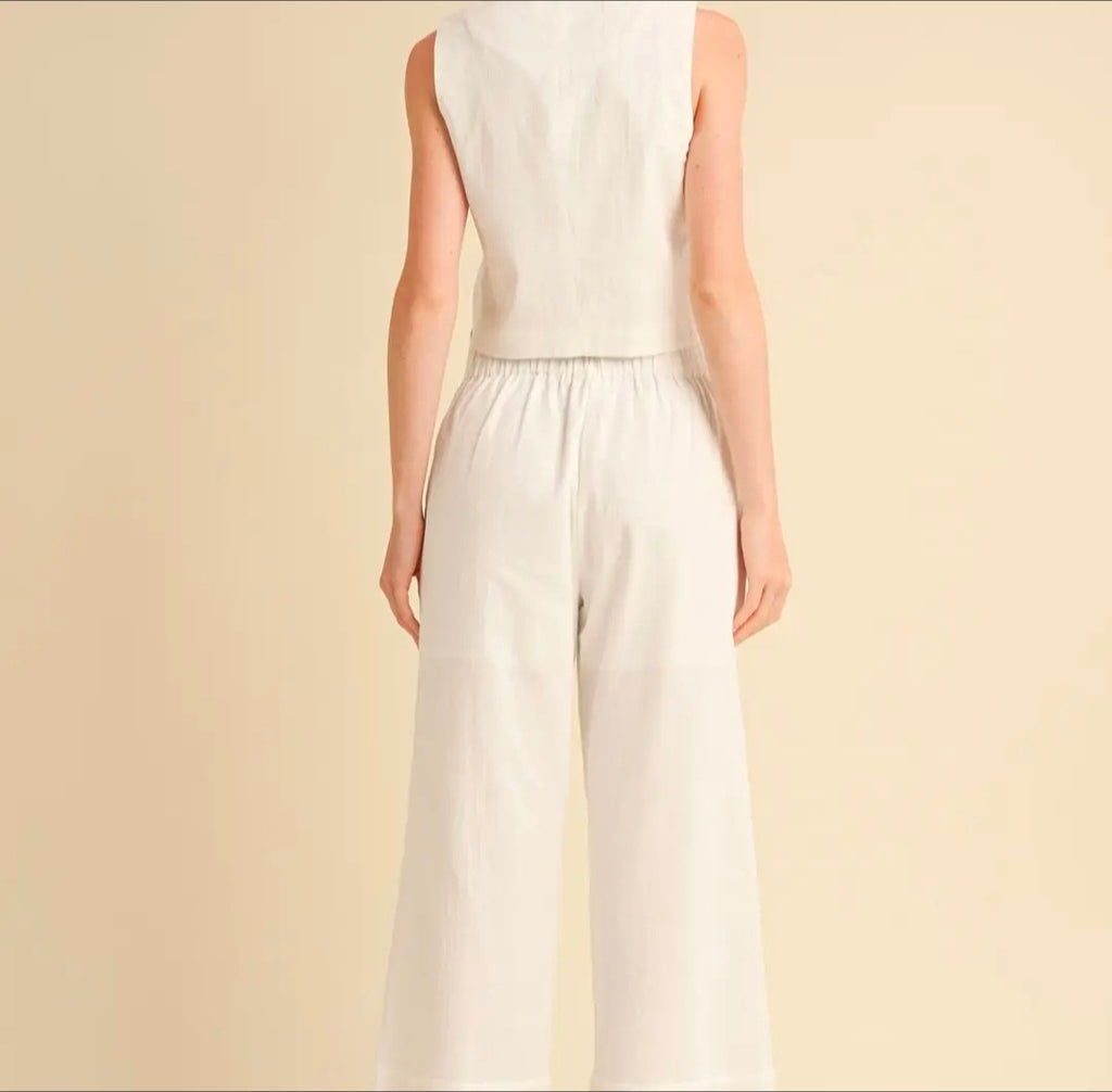 Person wearing a white sleeveless top and wide-leg pants on a beige background