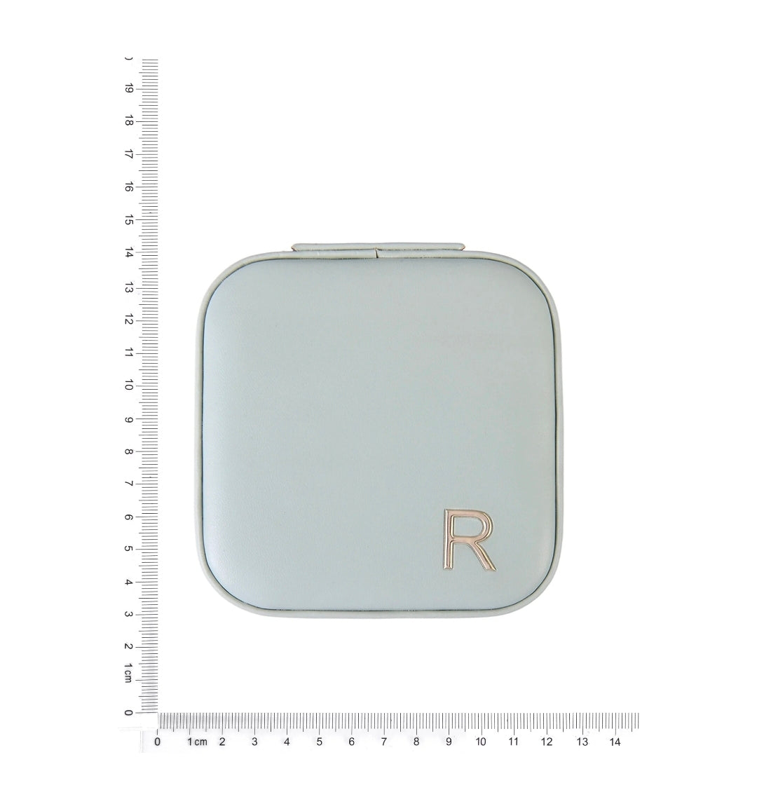 A square compact case with rounded corners in a pale blue-gray color, featuring a metallic rose gold 'R' monogram on the bottom right. The compact is shown on a white background with a black ruler on the left and a white ruler at the bottom to indicate its dimensions.