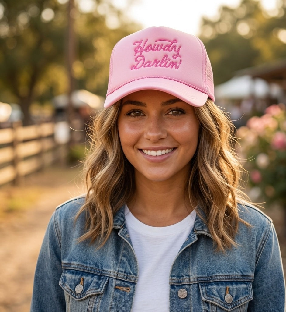 Woman wearing a pink cap with 'Howdy Darlin'' text, standing outdoors.