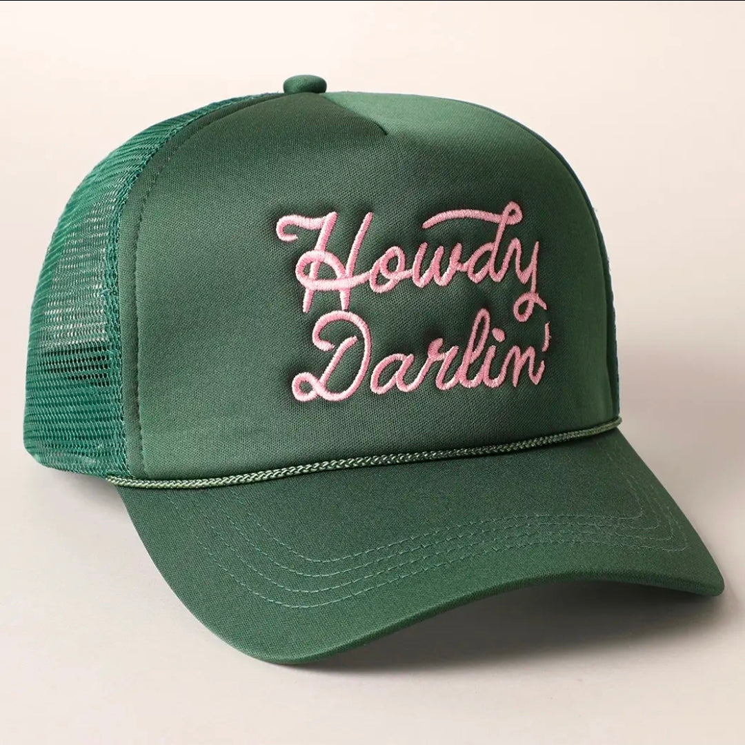 A green trucker-style baseball cap with pink embroidered cursive text reading 'Howdy Darlin'' on the front, shown against a plain light background.