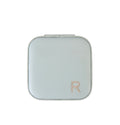 A square compact case with rounded corners in a pale sage green color, featuring a metallic rose gold letter 'R' logo in the bottom right corner, set against a plain white background.