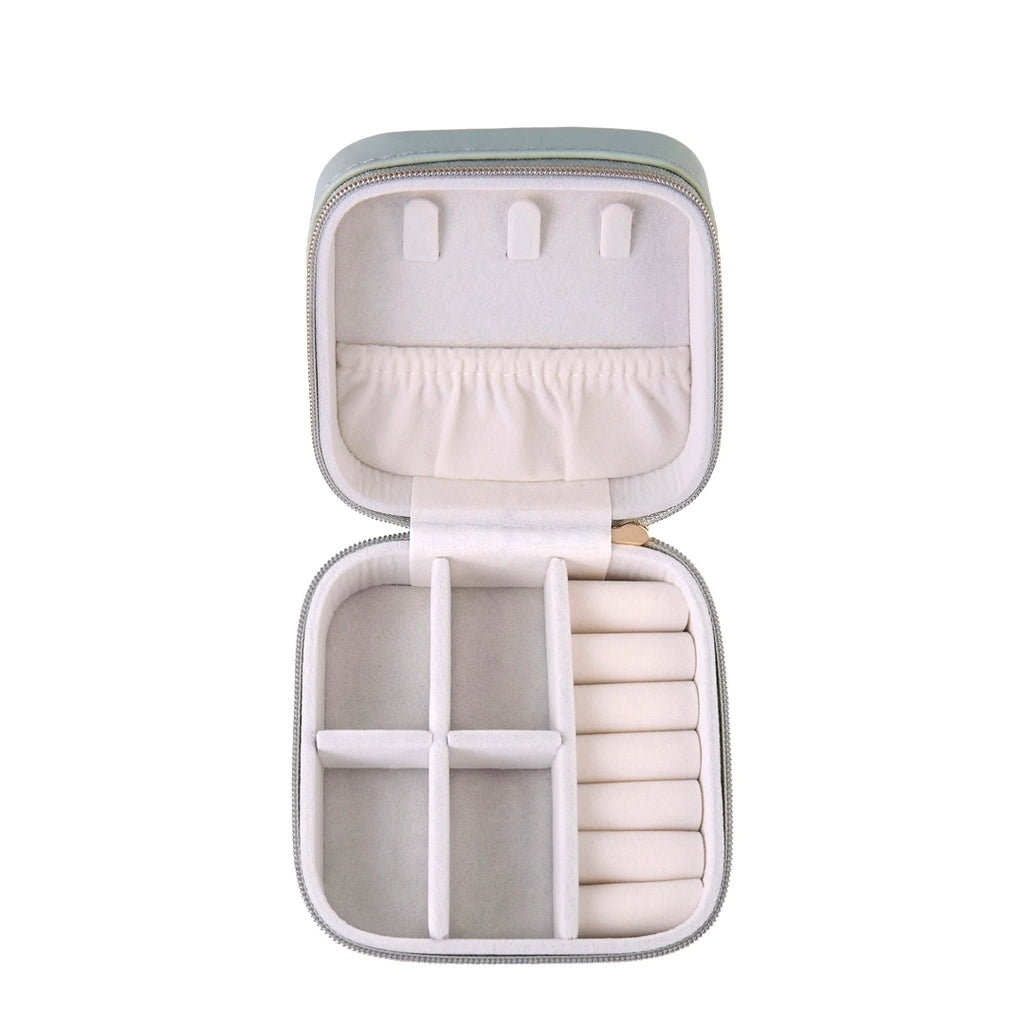 An open zippered jewelry organizer case with a light sage green exterior and cream-colored interior compartments, shown on a solid white background.