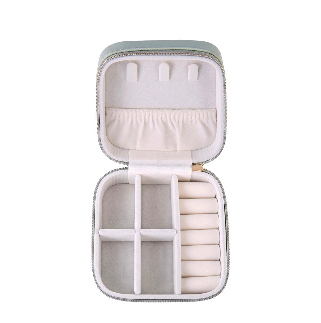 An open zippered jewelry organizer case with a light sage green exterior and cream-colored interior compartments, shown on a solid white background.