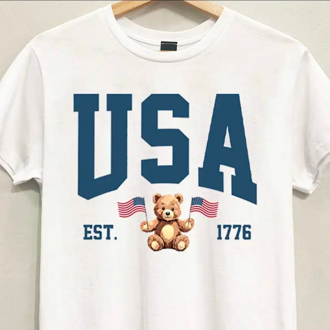 White t-shirt with 'USA' text and teddy bear graphic on a hanger.