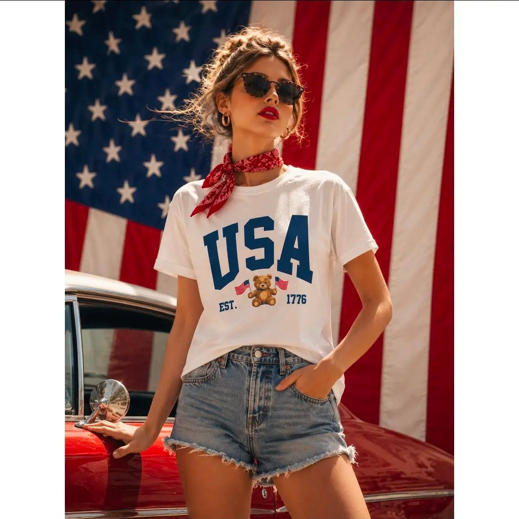 Woman wearing a 'USA' t-shirt with a teddy bear graphic in front of an American flag and classic car.